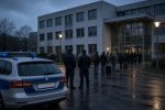 Streifenwagen und zwei Polizisten vor einer Behörde in der Dämmerung, Symbolbild zu Abschiebungen und Personalmangel